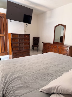 A bedroom with a bed, dresser, chair, and a television mounted on the wall. - Ground-floor apartment at "Sun House" (Puerto Vallarta)