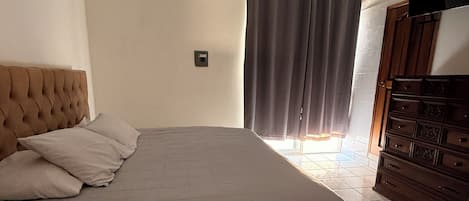 Een slaapkamer met een bed, een plafondventilator, een raam met gordijnen en een dressoir.