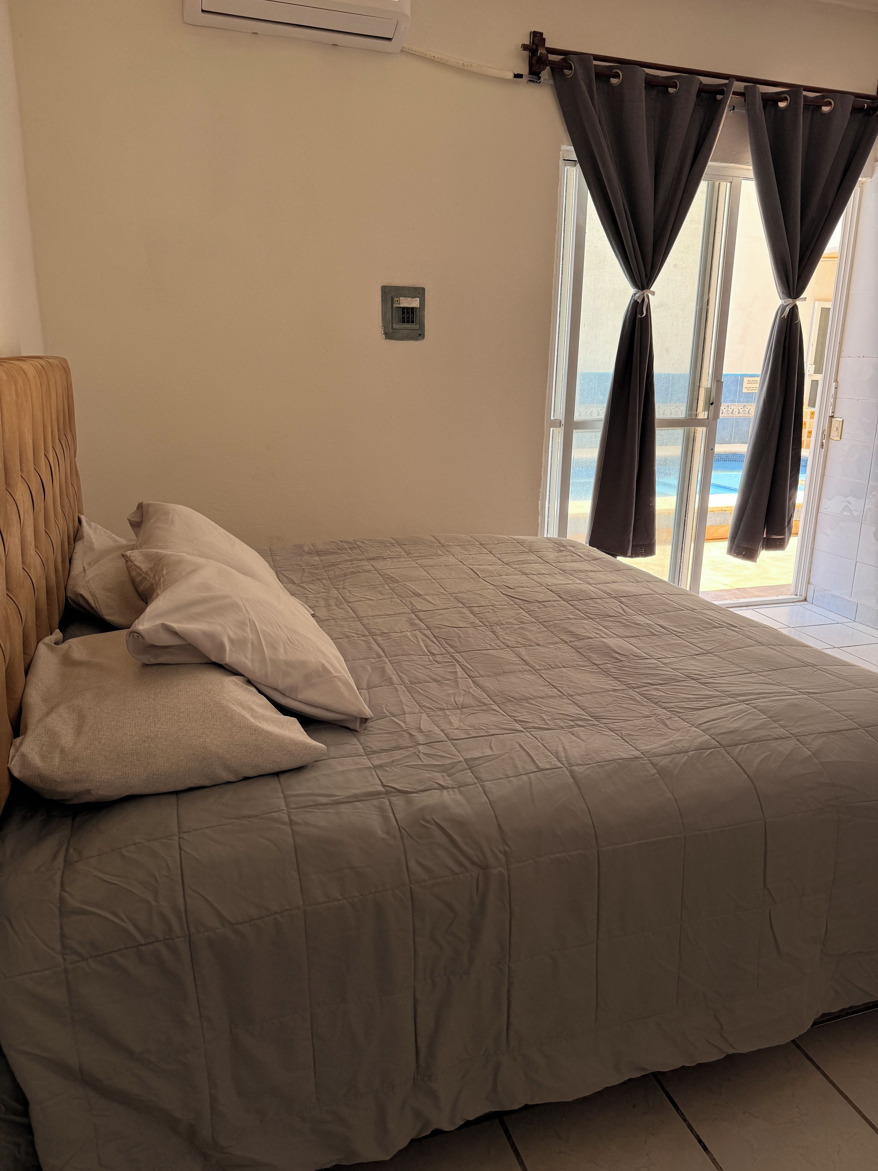 Ein Schlafzimmer mit einem Bett, Kissen, einem Kopfteil und einem Fenster mit Vorhängen.