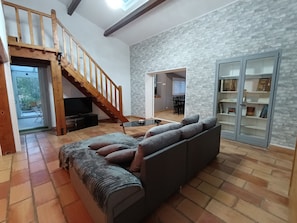 A spacious living area with a grey sofa, a wooden staircase, a television, and a bookshelf. - Maison de Campagne 9 places (Lançon-Provence)