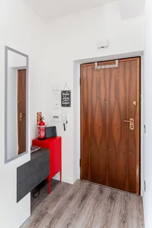 A hallway with a wooden door, a red cabinet, a fire extinguisher, and a wall-mounted light fixture.