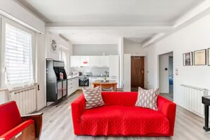A modern living room with a red sofa, a wooden chair, and a kitchen in the background.