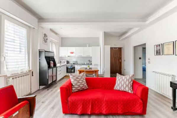 A modern living room with a red sofa, a wooden chair, and a kitchen in the background.