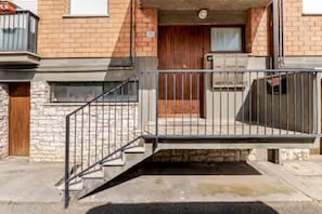 A building with a stone facade, a wooden door, and a metal staircase leading to a balcony.