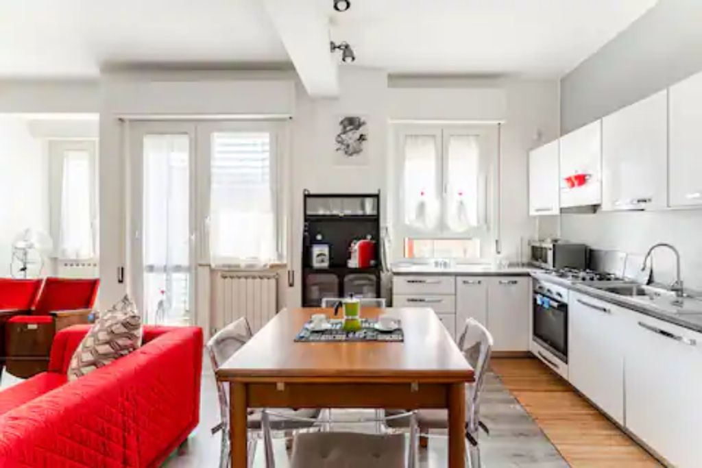 Eine moderne Küche mit weißen Schränken, einem Esstisch mit Stühlen und einem roten Sofa.