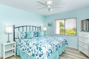 Un dormitorio con cama, lámparas de noche, ventilador de techo, ventana con persianas y cómoda.