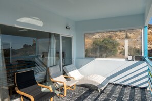 A sunlit room with a glass partition, two chairs, a small table, and a view of a natural landscape. - Sea and Silence Sea View Apartment - 2 minutes walk to the beach (Kalamaki)