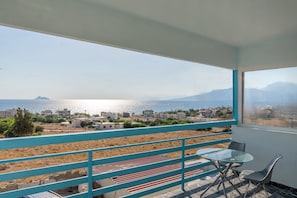 A balcony with a view of a coastal town, a table with a chair, and a striped rug. - Sea and Silence Sea View Apartment - 2 minutes walk to the beach (Kalamaki)