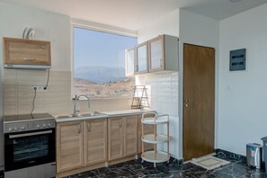 A modern kitchen with a built-in oven, a sink, wooden cabinets, and a window with a view of the mountains. - Sea and Silence Sea View Apartment - 2 minutes walk to the beach (Kalamaki)