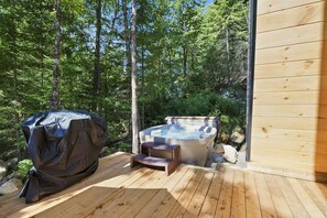 A wooden deck with a hot tub and a covered grill area, surrounded by a forest. - Spa & Nature | Celestra (Grenville-sur-la-Rouge)
