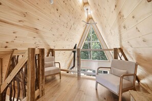 A wooden interior with a sloped ceiling, two chairs, and a window. - Spa & Nature | Celestra (Grenville-sur-la-Rouge)