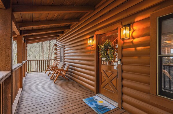 A wooden cabin with a porch, a door with a decorative pattern, and two wall-mounted lanterns. - Welcome to Sunset Vista! Endless Views + Hot Tub + Fire Pit + Game Room (Townsend)