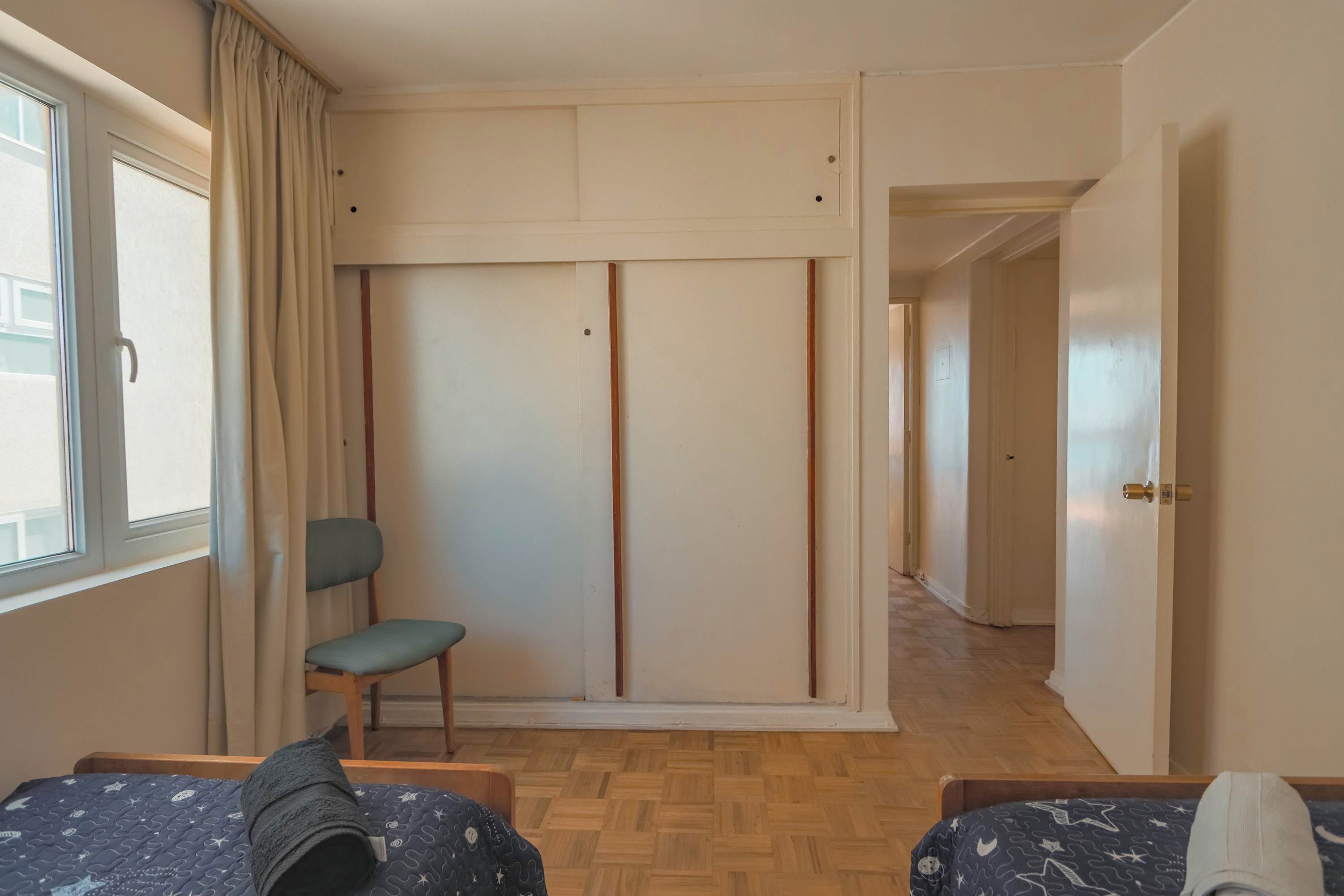 Un dormitorio con cama, una silla, un armario y un ventanal.
