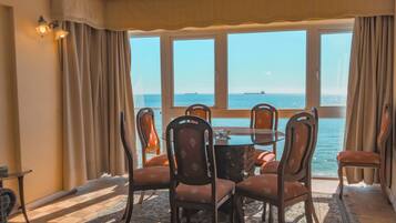 A dining area with a table and chairs, large windows with a view of the sea, and a patterned rug on the floor.