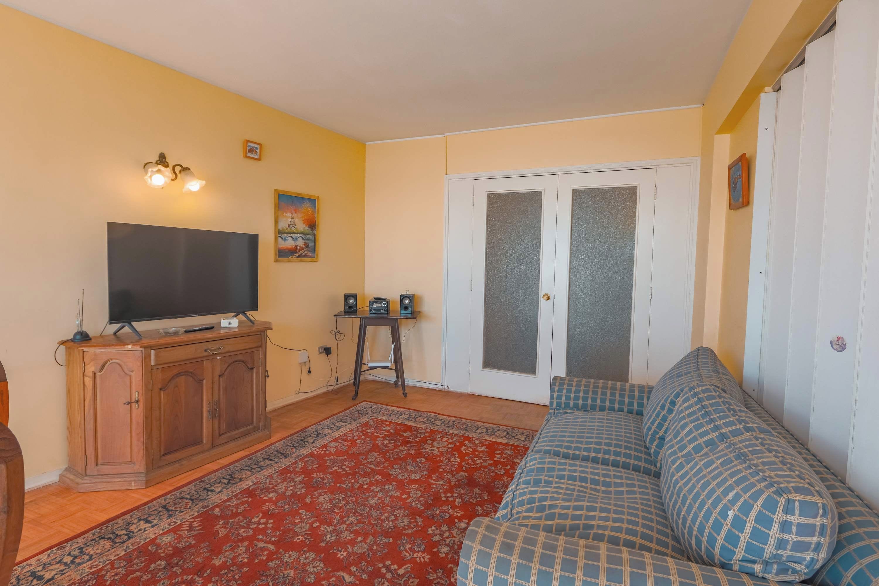 Una sala de estar con un sofá, un televisor, un aparador y una puerta con paneles de vidrio esmerilado.