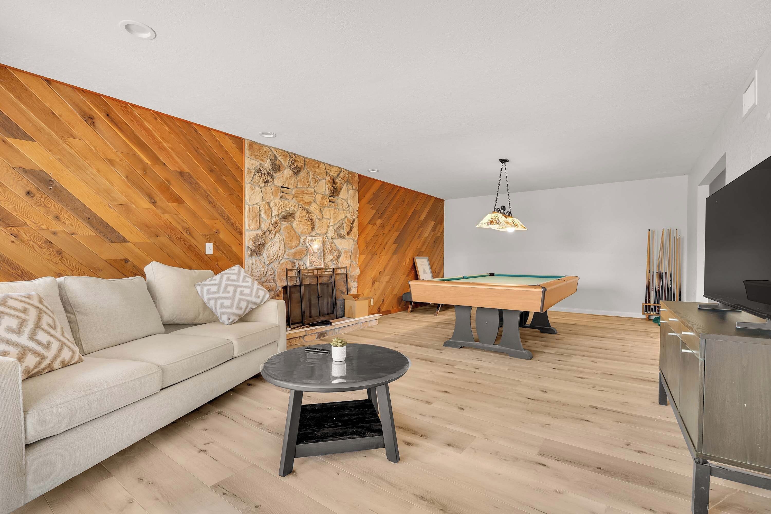 A modern living room with a wooden wall, a pool table, a sofa, and a television.