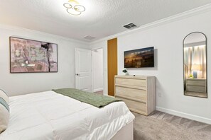 A bedroom with a bed, a dresser, a mirror, and artwork on the walls. - Themed Family Getaway, Private Pool, Top Location (Kissimmee)