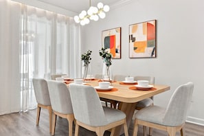 A modern dining room with a wooden table, grey upholstered chairs, and two abstract paintings on the wall. - Themed Family Getaway, Private Pool, Top Location (Kissimmee)