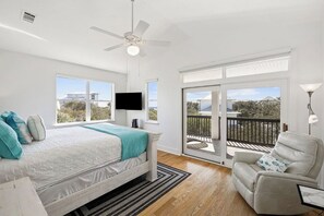 Een slaapkamer met een bed, een plafondventilator, een televisie, een balkon met uitzicht en een stoel.
