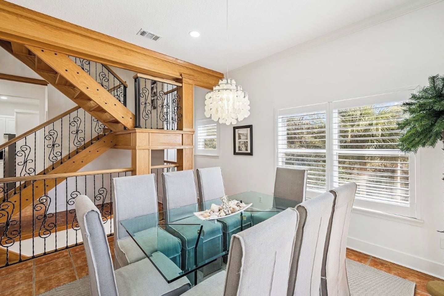 Un comedor con una mesa y sillas de vidrio, una escalera con barandillas de madera y un candelabro.