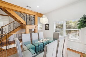 Een eetgedeelte met een glazen tafel en stoelen, een trap met houten leuningen en een kroonluchter.