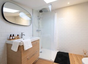 Un baño moderno con ducha de vidrio, tocador de madera con espejo y lavamanos blanco.