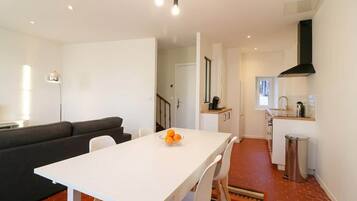 Une cuisine moderne avec un plan de travail blanc, une hotte noire et un coin repas comprenant une table et des chaises blanches.