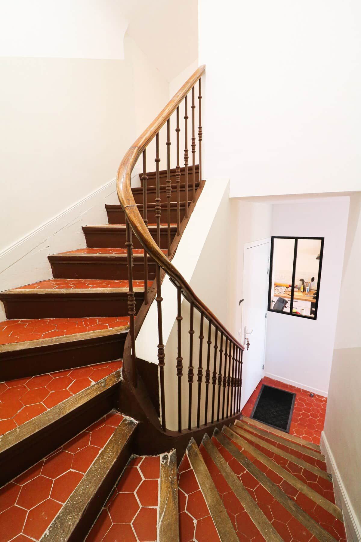 Een wenteltrap met houten treden en een zwarte metalen balustrade, leidend naar een deur met een raam.