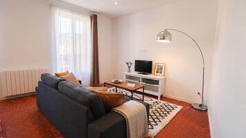 Un salon avec un canapé, un téléviseur, une lampe sur pied et un tapis à motifs.