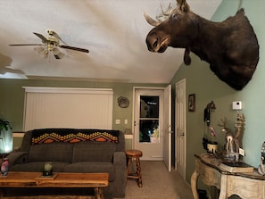A living room with a mounted moose head, a ceiling fan, a sofa with a patterned throw, a coffee table, and a door with a glass panel. - Beautiful Mountain Views! 3 Bed / 2 Bath house overlooking Pebble Creek Ski Hill (Inkom)