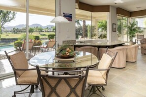 Un espace repas avec une table et des chaises en verre, un coin cuisine avec un bar, et une vue sur un terrain de golf.