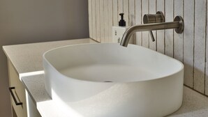 En hvid, oval vask med ét armatur monteret på en væg med lodrette linjer.
