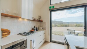 A modern kitchen with a gas stove, white cabinets, and a view of a landscape through a glass door.