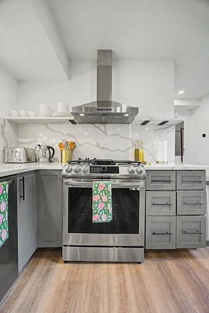 A modern kitchen with a stainless steel stove, oven, and a range hood. There are cabinets, a countertop, and a backsplash. - Lockwood Luxe - Arcade, Axe Throwing, Firepit, Two Kings (Atlanta)