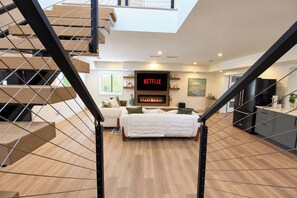 A modern living room with a fireplace, a flat-screen TV, and a staircase leading to an upper level. - Lockwood Luxe - Arcade, Axe Throwing, Firepit, Two Kings (Atlanta)