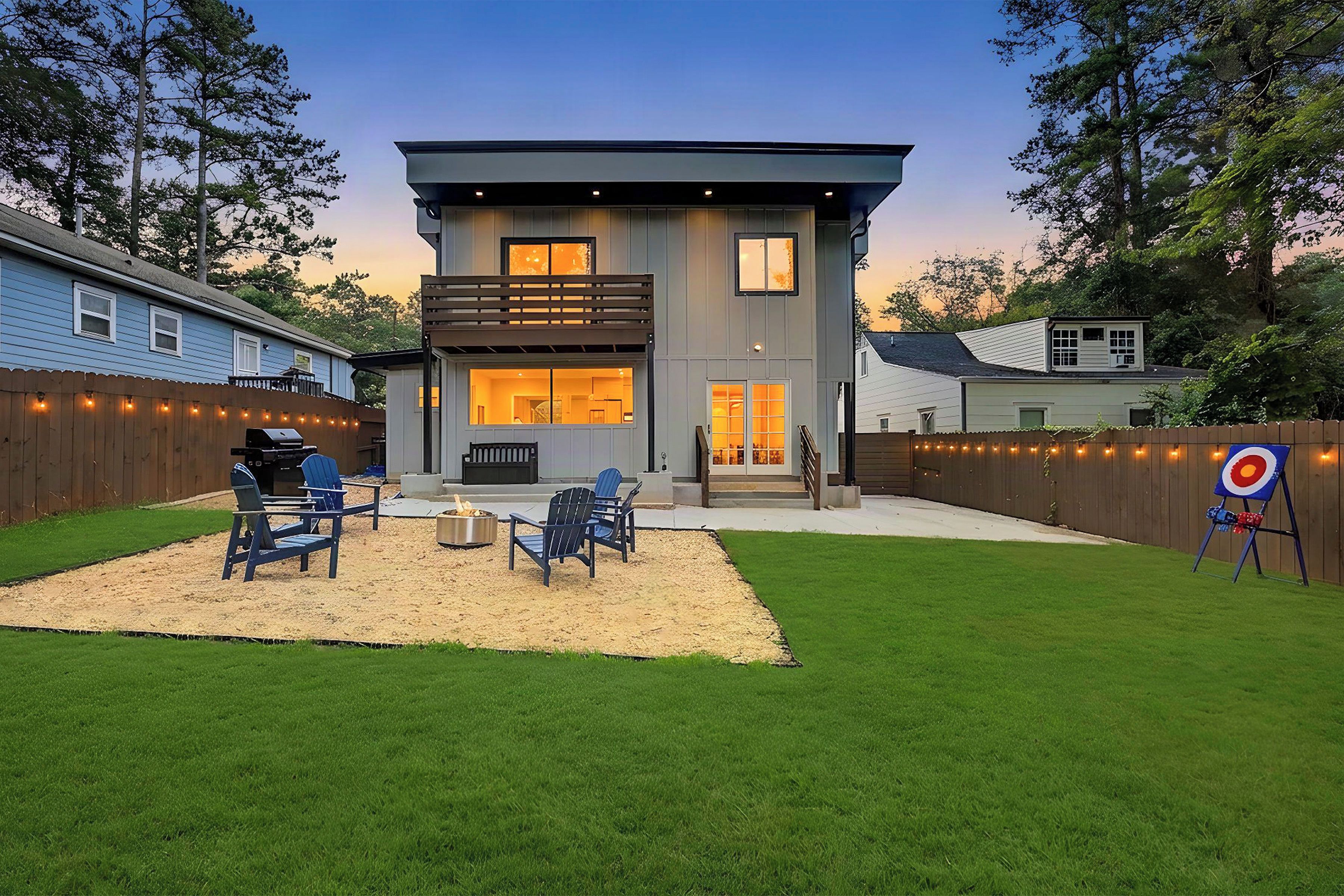 A modern two-story house with a backyard patio, outdoor seating, and a target for archery.