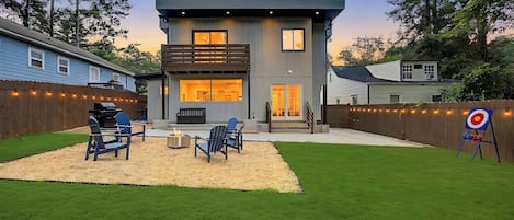 A modern two-story house with a backyard patio, outdoor seating, and a target for archery.
