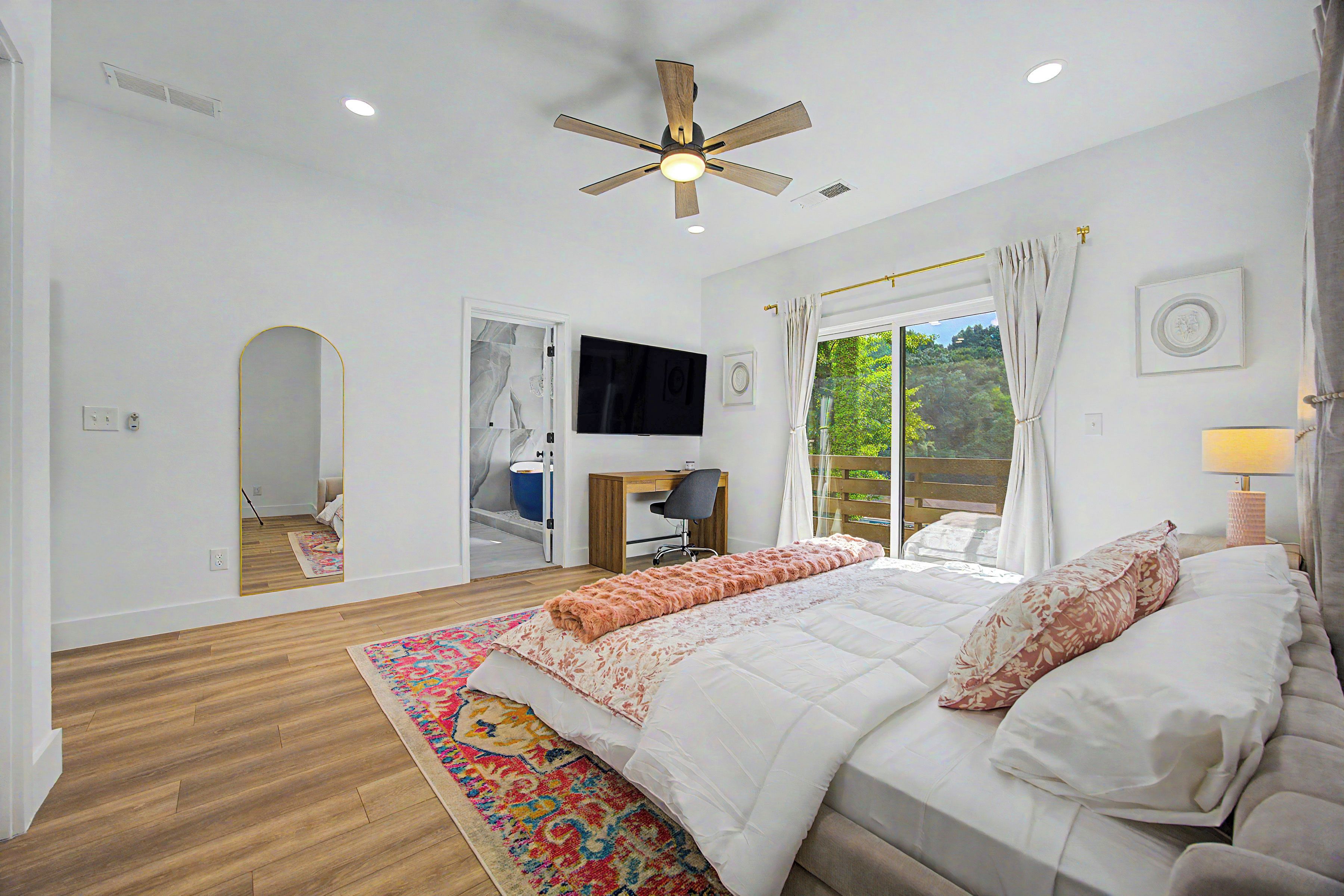 A bedroom with a bed, a desk, a television, and a window with curtains.