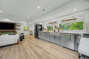 Een moderne keuken met roestvrijstalen apparatuur, houten vloeren en een groot raam met uitzicht op groen.