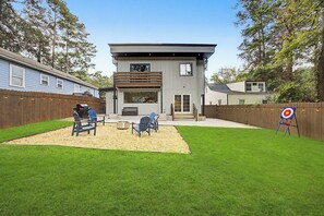 Een modern huis met twee verdiepingen, een terras, buitenmeubels en een doel op het gazon.