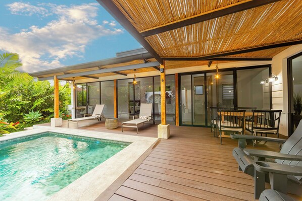 A modern outdoor pool area with a wooden deck, lounge chairs, and a glass-enclosed patio. - Casa Volcancito- Volcan View (Provincia de Alajuela)