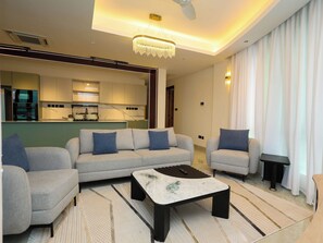 A modern living room with a sofa set, a coffee table, and a dining area with a kitchen in the background. - 2 bedroom beachfront in Nyali with infinity pool, sauna, gym & near malls (Mombasa)