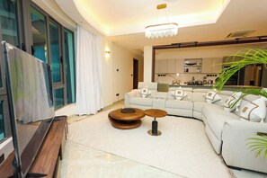 A modern living room with a large flat-screen TV, a sectional sofa, a coffee table, and a kitchen in the background. - 2 bedroom beachfront in Nyali with infinity pool, sauna, gym & near malls (Mombasa)