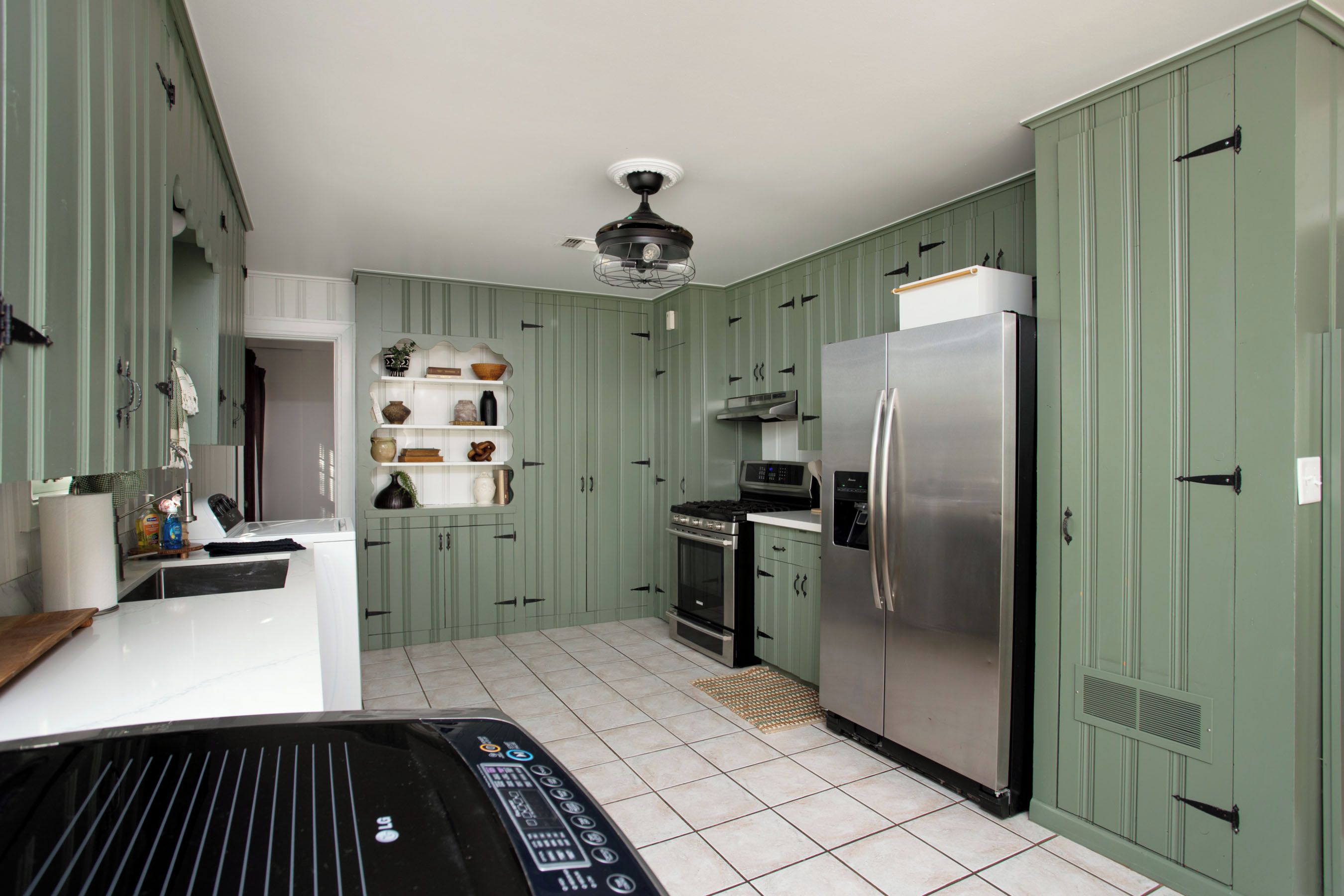 Una cocina con gabinetes verdes, un refrigerador de acero inoxidable, un microondas y una estufa a gas.