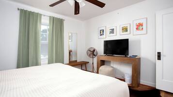 A bedroom with a bed, a ceiling fan, a TV on a wooden stand, and artwork on the wall.