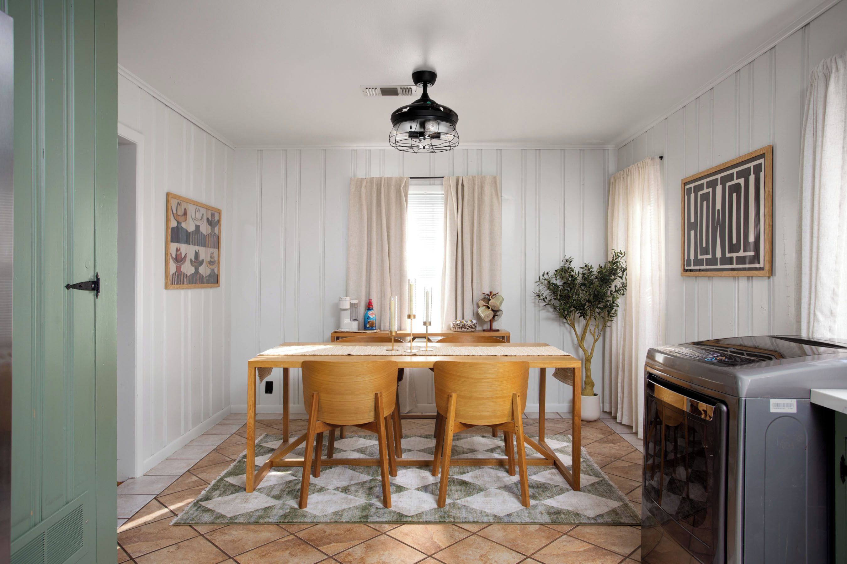 Uma sala de jantar com mesa de madeira, duas cadeiras, um ventilador de teto e uma cozinha com fogão.