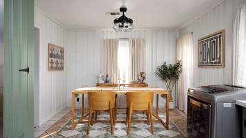 Uma sala de jantar com mesa de madeira, duas cadeiras, um ventilador de teto e uma cozinha com fogão.