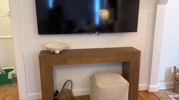 A flat-screen TV mounted on a wall above a wooden console table with a woven basket and a small stool.