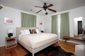 Quarto com cama, mesa de cabeceira, luminária, ventilador de teto e espelho.