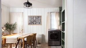 A dining area with a wooden table and chairs, a wall-mounted light fixture, and a window with curtains. - Choosing Texas (Amarillo)